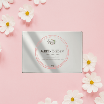 Coffret cadeau Fondants Parfumés fermé Jardin d'Éden. Boîte blanche et argentée sur fond rose avec fleurs blanches. Thème Floral, Kit Découverte.