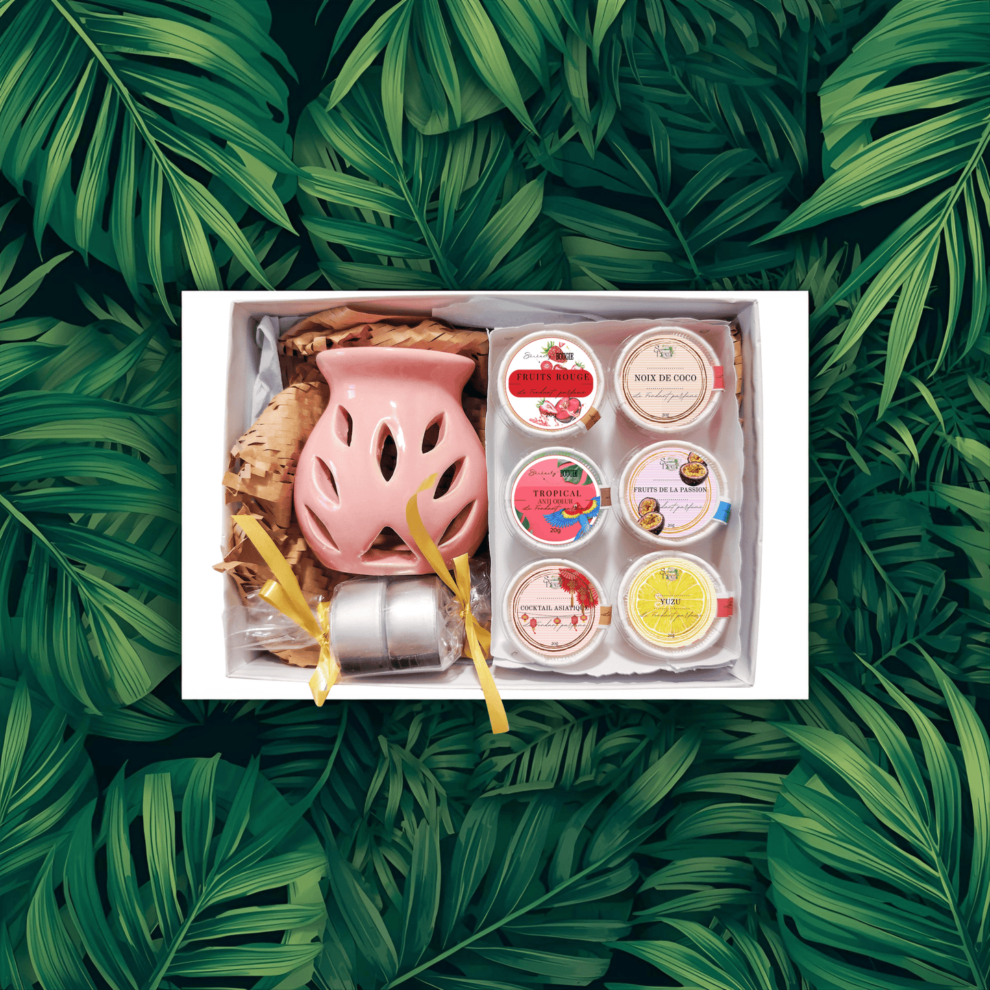 Coffret Fondants Parfumés "Évasion Tropicale" ouvert sur fond de feuilles de palmier. Contient un brûle-parfum rose, deux bougies, et 6 fondants aux parfums fruités : Noix de Coco, Fruit de la Passion, Yuzu, Cerise Noire, Fruits Rouges, Cocktail Asiatique. Cire végétale.
