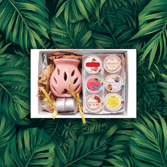 Coffret Fondants Parfumés "Évasion Tropicale" ouvert sur fond de feuilles de palmier. Contient un brûle-parfum rose, deux bougies, et 6 fondants aux parfums fruités : Noix de Coco, Fruit de la Passion, Yuzu, Cerise Noire, Fruits Rouges, Cocktail Asiatique. Cire végétale.
