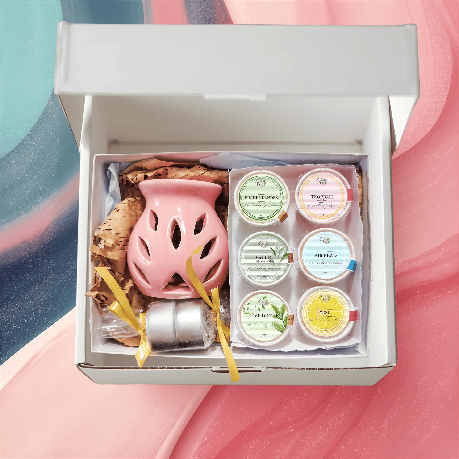 Coffret Fondants "Best Sellers Les Essentiels" ouvert. Contient un brûle-parfum rose, deux bougies, et 6 fondants aux parfums variés : Linge Frais, Caramel Beurre Salé, Fleur de Sakura, Cerise Noire, Pin des Landes, Ambre Gris. Cire végétale artisanale.