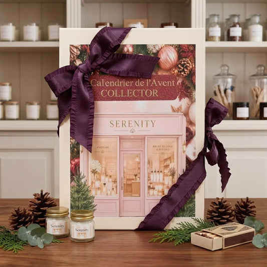Un grand coffret vertical en carton beige clair avec un couvercle illustré. L'illustration représente la façade d'une boutique "SERENITY" élégante et décorée pour Noël, avec des vitrines illuminées affichant des parfums, des brumes de linge et des bougies. Le texte "Calendrier de l'Avent COLLECTOR" est écrit en doré et bordeaux sur la partie supérieure.
