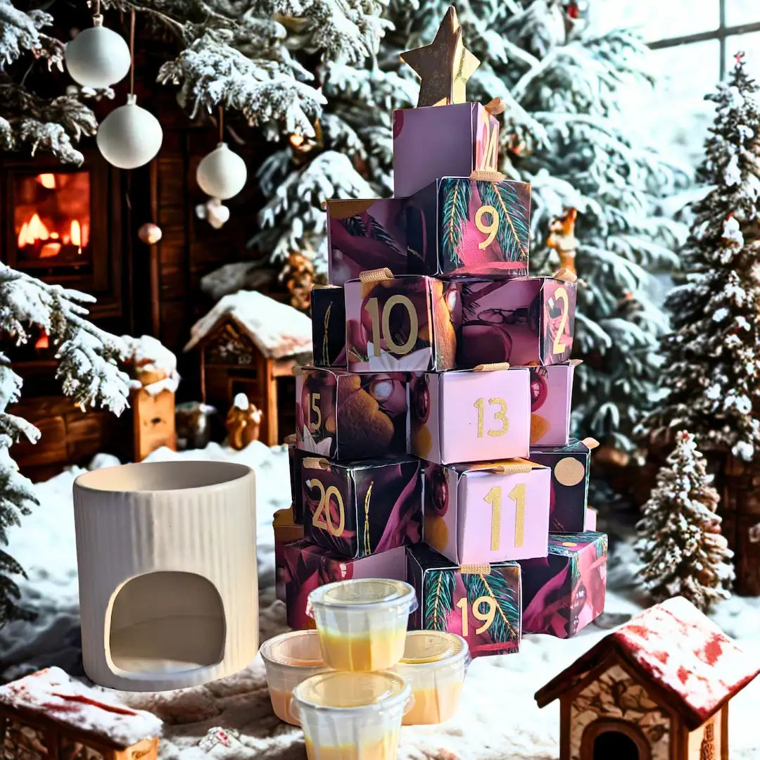 Une scène de Noël enchantée et enneigée mettant en scène le calendrier de l'Avent Serenity Bougie. Le calendrier est construit en forme de sapin de Noël avec des boîtes cadeaux numérotées et colorées (rose, rouge, noir), coiffé d'une étoile dorée. À sa base se trouvent un diffuseur d'huile en céramique blanche et une pile de petits pots de bougies en cire empilés. L'arrière-plan comprend des sapins enneigés décorés de boules blanches, une cheminée allumée et des maisons miniatures de Noël, créant une atmosp